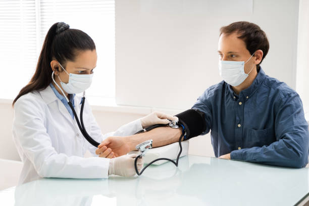 Doctor Checking High Blood Pressure Doctor Checking High Blood Pressure In Face Mask hypertensive photos stock pictures, royalty-free photos & images