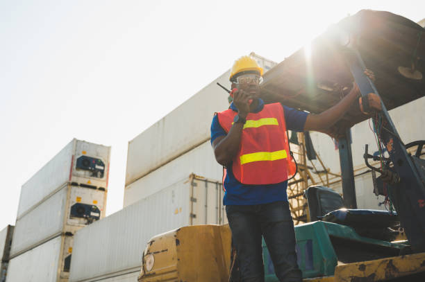 istock Black foreman worker working control the crane and forklift at Container cargo harbor to loading containers. African dock male staff with radio walkie-talkie for Logistics import export shipping concept. 1223738202