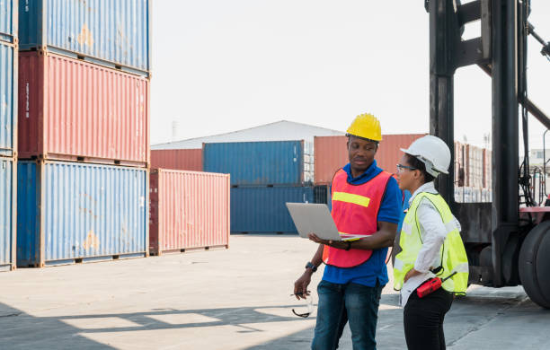 istock Two Black foreman man & woman worker working checking at Container cargo harbor holding laptop computer and using walkie-talkie to loading containers. African dock male and female staff business Logistics import export shipping concept. 1223738366