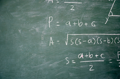 The male teacher used white chalk to write on the blackboard to teach students in a class.