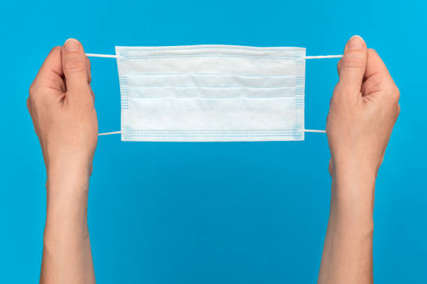 istock Woman's hands holding medical mask on blue background. 1223741679