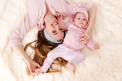 Smiling mother and baby girl in pink lying on their back, top view. mother and daughter photo shoot