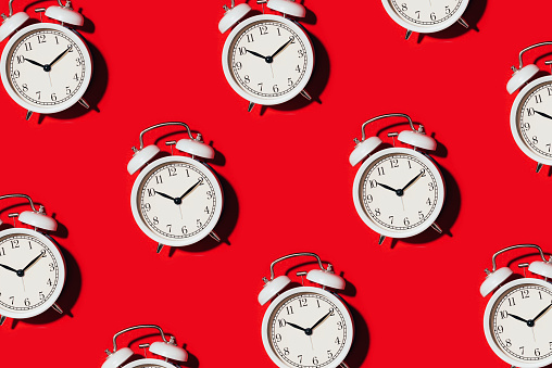 Pattern of white alarm clock on red background. Wake up alert concept. Morning routine. Back to school concept. Minimalist style design. Packing design. Creative design, minimal flat lay concept.