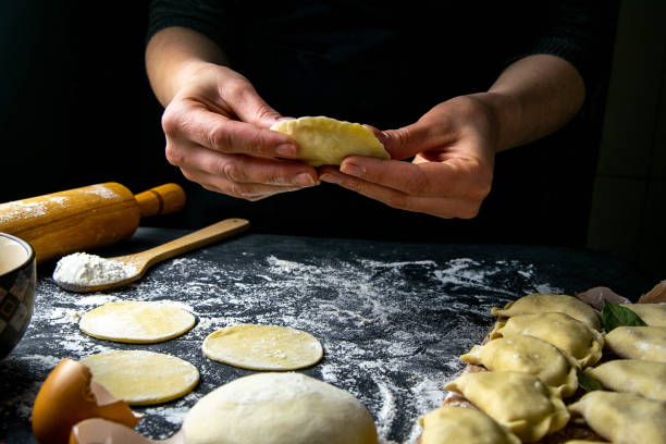 istock Cook in a dark jacket prepares dumplings. over a dark table on which the finished dumplings are laid out. Front views, close-up 1223760536