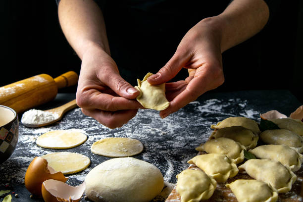 istock Cook in a dark jacket prepares dumplings. over a dark table on which the finished dumplings are laid out. Front views, close-up 1223760540