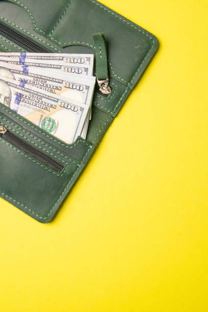 istock Several hundred dollar bills protrude from a stylish green leather wallet on a bright yellow background. Top view with clear space 1223760740