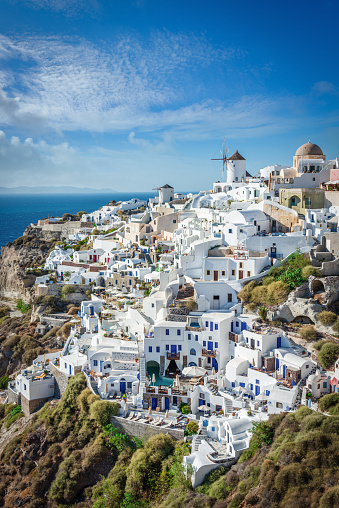 Scenic view towards Oia with the iconic white and blue typical greek Santorinia Houses, Windmill and orthodox church at the rocky mediterranean coast of Santorini. Oia, Santorini Island, Cyclades Islands, Greece, Europe.