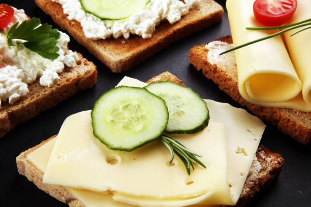 rolled slices of golden gouda cheese or cream cheese on a sandwich garnished with sliced cucumber and herbs. bread or toast with cheese for breakfast