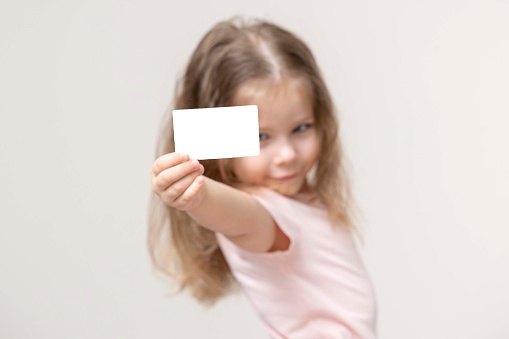 little girl holds a card in front of her and smile, portrait, copy space. advertising space. empty white business card