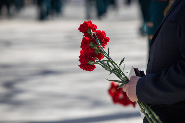 istock A hand puts red carnations on a granite gravestone. Memory of the dead 1223768004