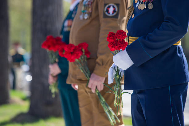 istock A hand puts red carnations on a granite gravestone. Memory of the dead 1223768419