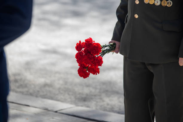 istock A hand puts red carnations on a granite gravestone. Memory of the dead 1223768690