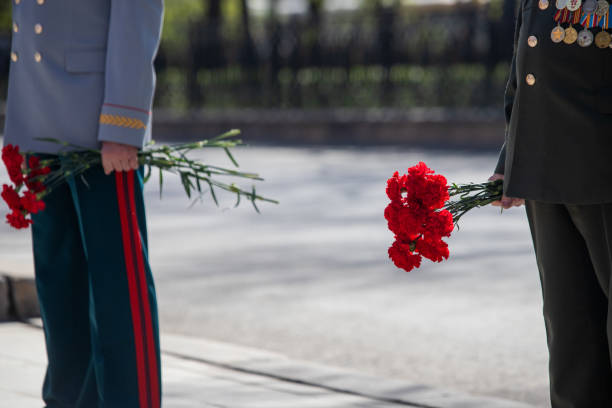 istock A hand puts red carnations on a granite gravestone. Memory of the dead 1223768759