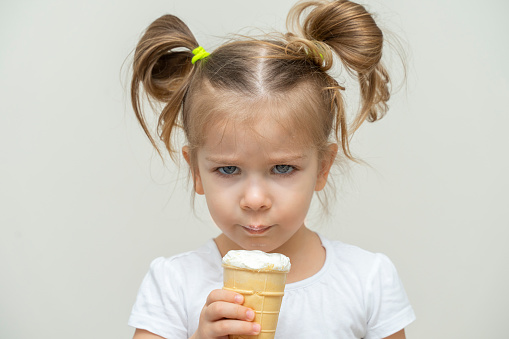 3-4 years old girl in a white T-shirt eats ice cream and gets angry.piercing angry look at the camera