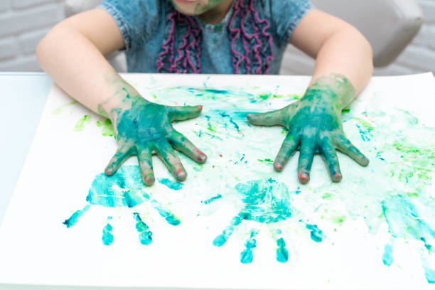 Little girl paints with fingers.girl makes fingerprints on the paper with her green palms in the paint, self-isolation, coronavirus covid-19, stay home