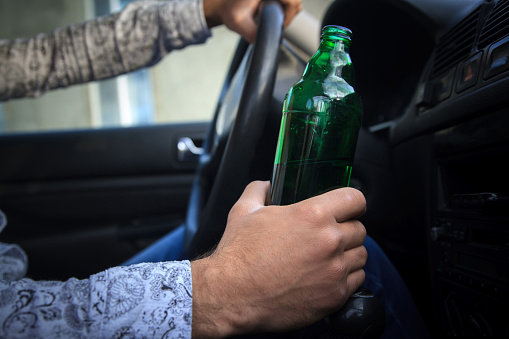 Drunk young man driving a car on the road with a bottle of beer.