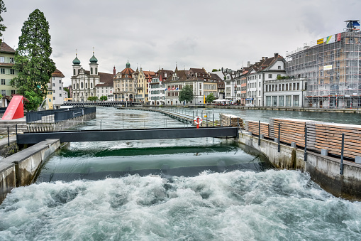 Lucerne, Switzerland - June 26, 2016. Needle dam in the River Reuss in Lucerne, Switzerland. This is one of the last remaining needle dams in the world. View with surrounding historic buildings, commercial properties and people.