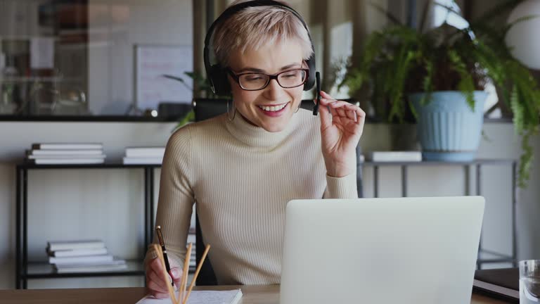 Smiling business woman wearing headset conference calling on laptop