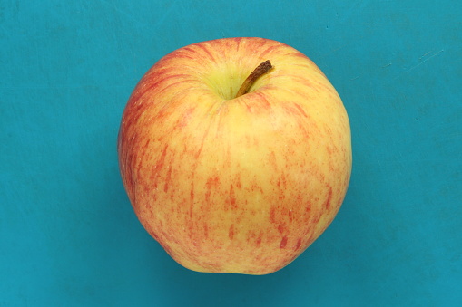 Red yellow apple on a blue background. Juicy ripe beautiful fruit.