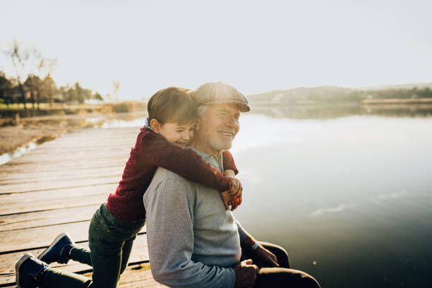 Grandfather and grandson on a lake dock Photo of grandfather and grandson on a lake dock grandchild stock pictures, royalty-free photos & images