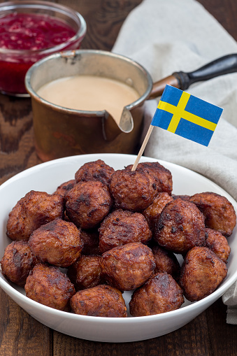 Meatballs served with cream sauce and cranberry jam,  in a white bowl with swedish flag, vertical