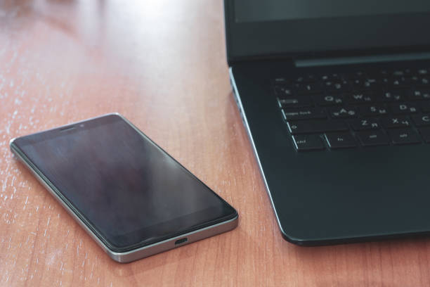 istock Black laptop and cell phone on the table. Selective shallow focus on the phone. Back light. Horizontal. 1223794051