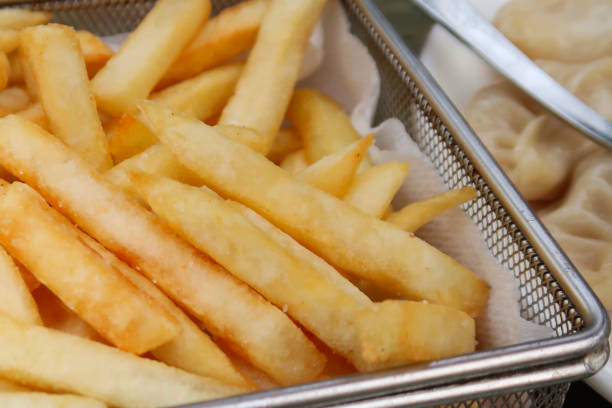 Stock photo of crispy chunky chips / French fries takeaway food at bar restaurant, unhealthy greasy snack food fried in peanut vegetable oil, served in metal basket, English takeaway chips ready to eat with salt and vinegar imagen de patatas fritas crujientes / papas fritas comida para llevar en el bar restaurante, bocadillos grasosas poco saludables fritos en aceite de verduras de maní, servidos en cesta de metal, patatas fritas inglesas listas para comer con sal y vinagre