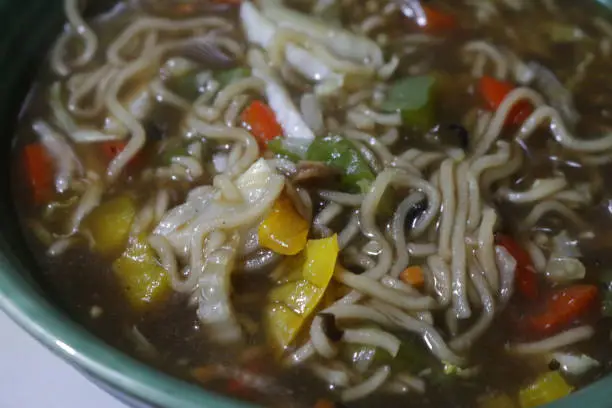 Stock photo showing an elevated view of a meal of homemade spicy thai noodle soup / broth in a green bowl. This is a low calorie meal made with chopped vegetables and rice noodles, which are low in carbohydrate. This dish is part of a healthy eating, low fat diet plan.