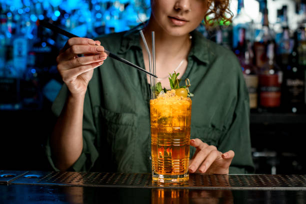 Woman using tweezers gently decorates cocktail by glass sticks
