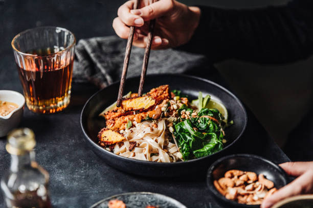 Woman eating freshly made Asian vegan meal Close-up of a woman eating food with chopsticks. Female eating freshly made Asian vegan meal. meat substitute stock pictures, royalty-free photos & images