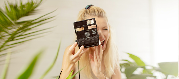 Young blonde girl photographing on polaroid, smiling. Hobby concept.