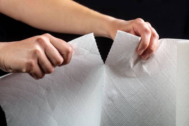 Hands tear off a piece of white paper towel from a roll on a black background. Horizontal orientation Hands tear off a piece of white paper towel from a roll on a black background. Horizontal orientation. High quality photo. paper towel stock pictures, royalty-free photos & images