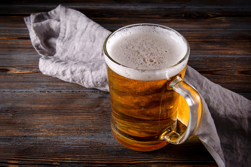 alcoholic beverage , 1 glass of light barley beer with foam on a gray napkin on a dark wooden background,