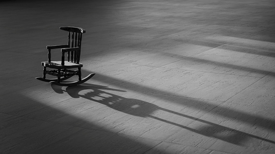 Sunlight and shadow on surface of the old vintage little wood rocking chair on wooden tile floor in black and white style, concept of loneliness, alone, thinking of people who have gone far far away