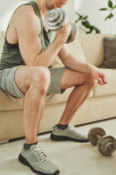 istock Young athlete in activewear holding metallic dumbbell while exercising on couch 1223817529