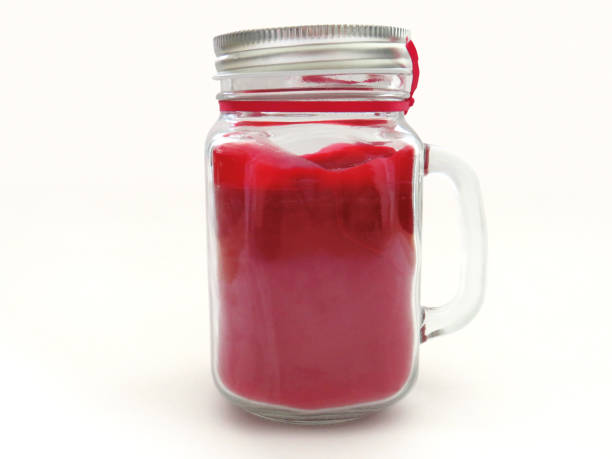 istock Raspberry scented candle in glass jar isolated on white background. Red burning candle in glass jar with lid to preserve fragrance. 1223823279