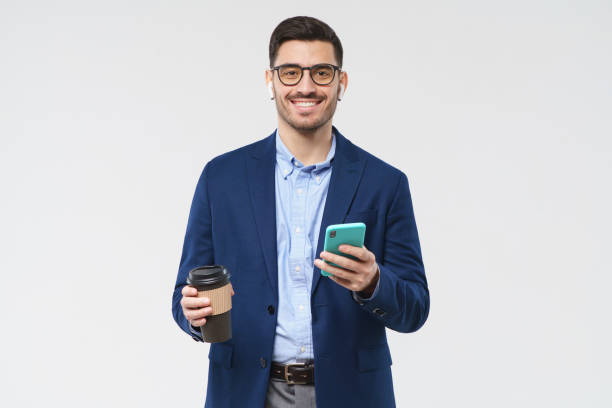 istock Young business man drinking coffee and chatting on phone during break from work, smiling happily, looking at camera, isolated on gray background 1223827342