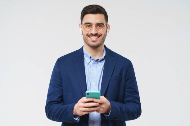 istock Young smiling business man holding smartphone in hands, communicating with colleagues, looking at camera, isolated on gray background 1223827343