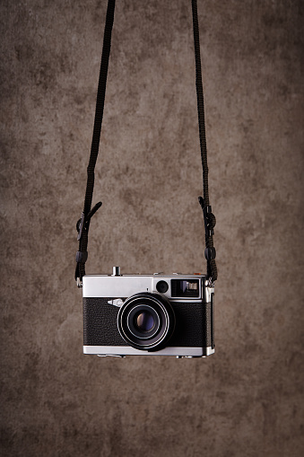 Vintage analog rangefinder film camera hanging in front of a concrete textured wall as background