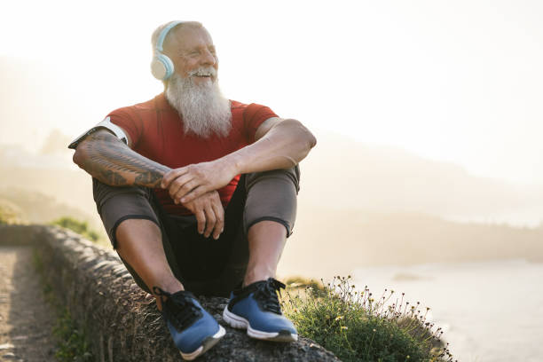 Senior fit man outdoor at sunset after workout session - Mature athlete training outside while listening playlist music with headphones - Sport and joyful elderly lifestyle concept