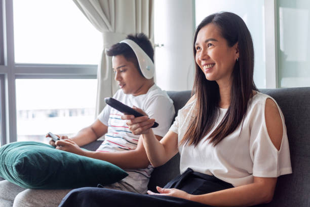 woman and man sitting on sofa, watching tv and playing mobile games - gamer watching tv adult couple imagens e fotografias de stock