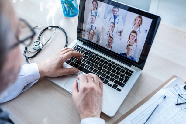 medico maschio in videoconferenza su laptop con i suoi colleghi a casa. - medicine lab coat hospital senior adult foto e immagini stock