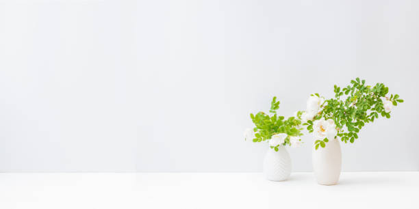istock Home interior with decor elements. White small flowers and green leaves in a vase on a light background 1223853033