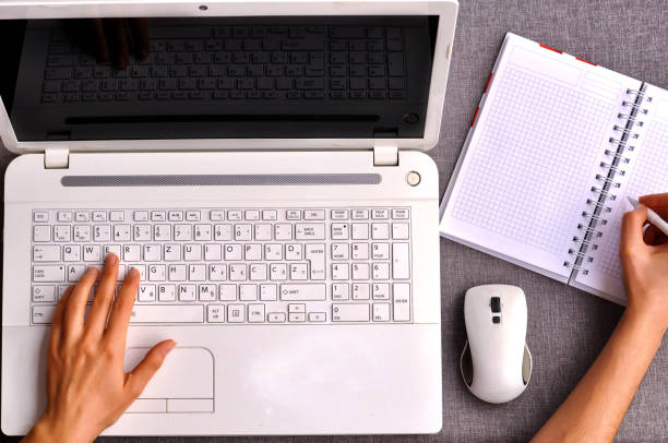 istock Human hands typing on a white laptop keyboard with isolated screen.Working desk table concept.High above view of office workplace with phone and mouse with notebook, pen and usb flash on grey desk. 1223856667