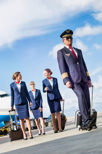 portrait of mature pilot walking with three young beautiful flight attendants against airplane in airport - cabin crew pilot airport walking imagens e fotografias de stock