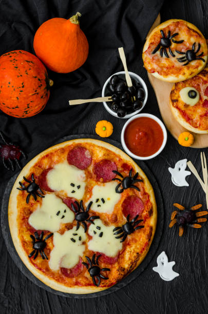 istock Halloween Pizza Monsters with cheese Ghost and olive Spider on a black background. Food idea for Halloween party. 1223859985