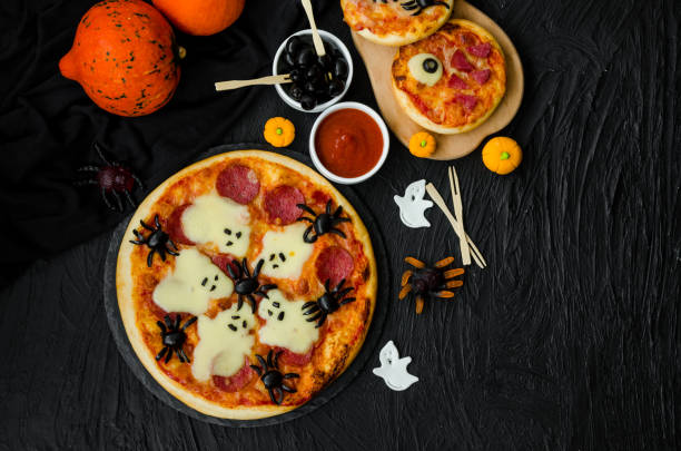 istock Halloween Pizza Monsters with cheese Ghost and olive Spider on a black background. Food idea for Halloween party. 1223859988