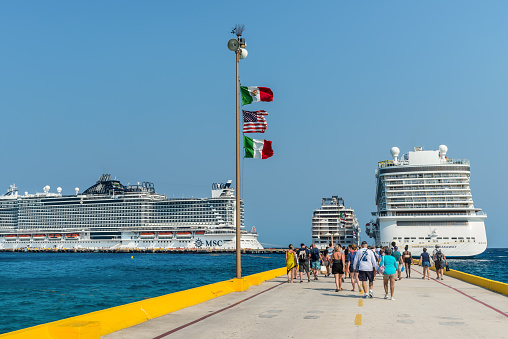 Costa Maya, Mexico - April 25, 2019: Three cruise ships side by side with passengers  return to ships at Costa Maya Port. Flags of Mexico, USA and Italy fluttering in the wind.