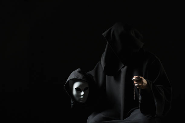 istock Vicious mage in black mantle and demon in sleeve. Ritual deal with devil. Man with split personality. Schizo talking to mask. Cursed assassin end evil spirit in dark room. Monk curse. Evil sorcerer. 1223863065