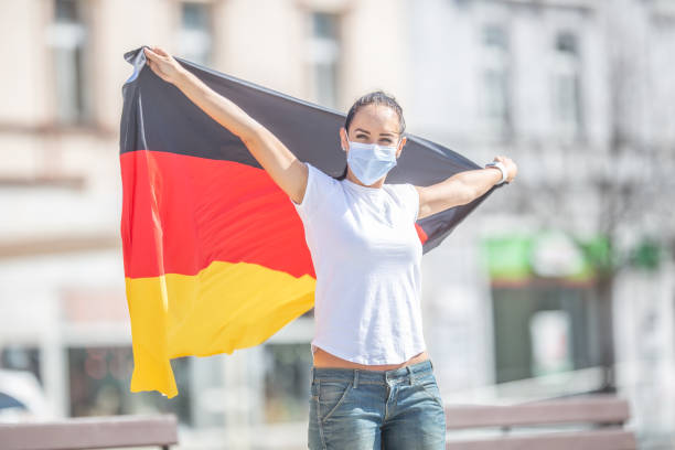 istock German fan in a face mask holds the flag behind her outdoors, smiling. 1223866079